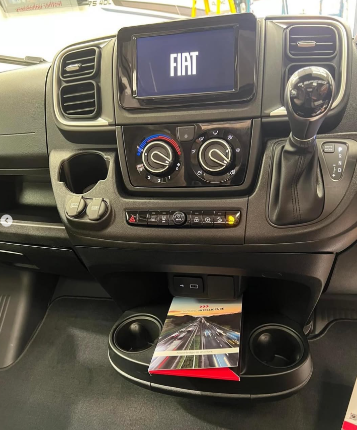 A Fiat motorhome dashboard with a Moving Intelligence leaflet in the cup holder.