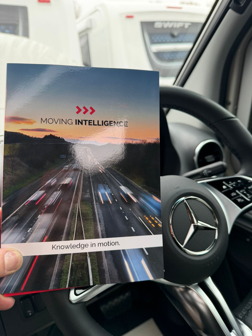 Person holding a brochure titled 'Moving Intelligence' in a car interior.