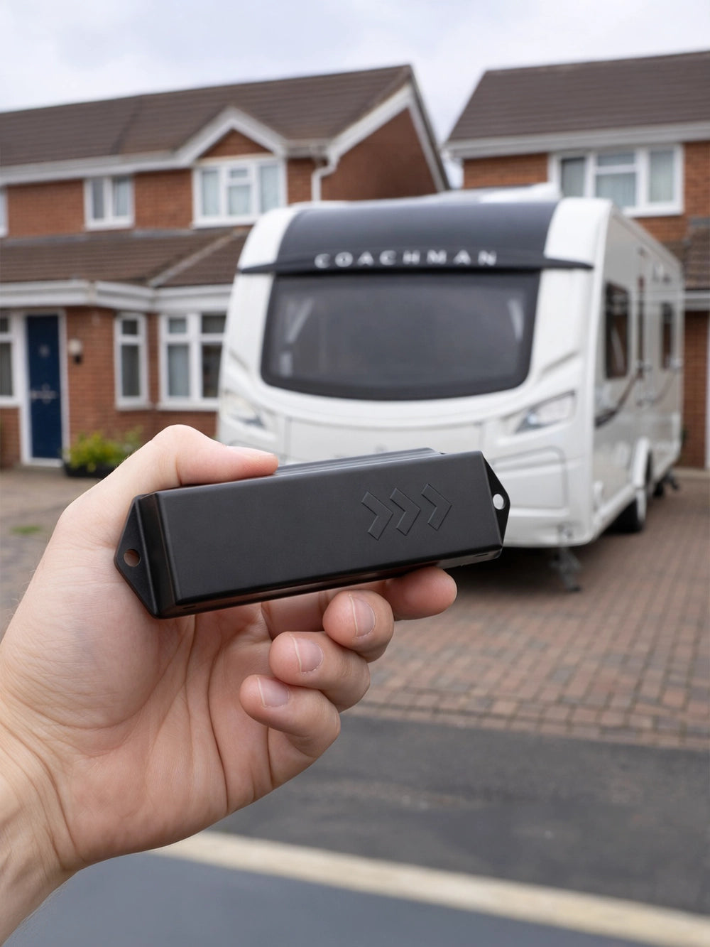 Hand holding a vehicle GPS tracking device with a Coachman caravan in the background