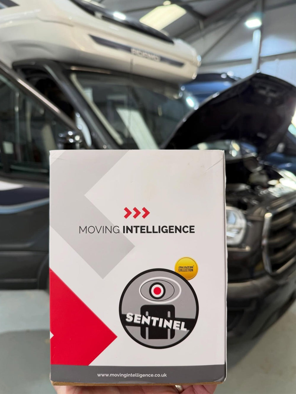 Box labeled 'Moving Intelligence Sentinel' held in front of a car interior.