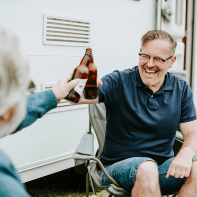 Two people having a drink and cheering outside their caravan enjoying their holiday while protected by Moving Intelligence state of the art trackers.