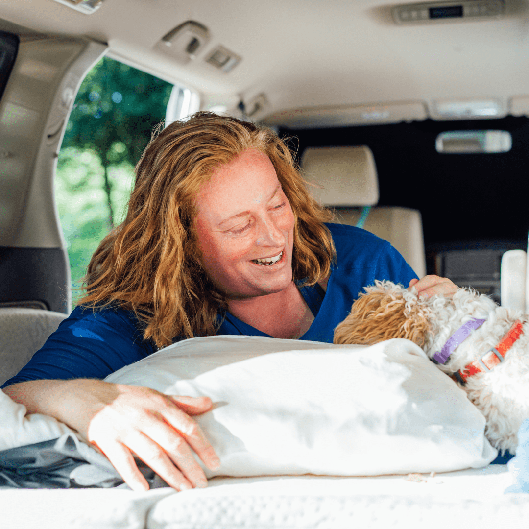 A happy woman lying in her motorhome with her dog with pet mode turned on which means the interior of the motorhome is well protected.