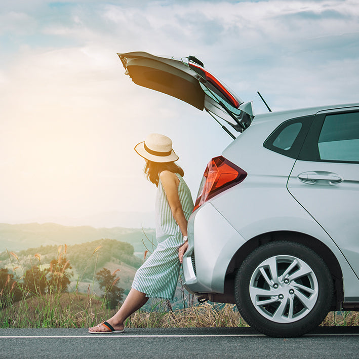 A woman sat on her car beside the road watching the sunset enjoying peace of mind because of her new tracker.